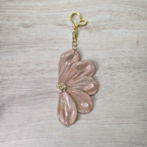 Charm de bolso con forma de media flor, compuesta de 5 pétalos en color moca con detalles iridiscentes El enganche tiene forma de corazón y es en color dorado