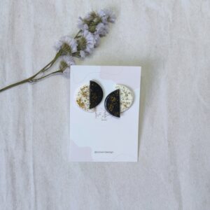 Pendientes compuesto por dos semi círculos, uno blanco y otro negro, ambos con brillantina en color oro