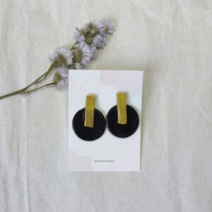 Pendientes compuesto de dos piezas, una circular en color negro con efecto cuero y una pieza central rectangular en color oro
