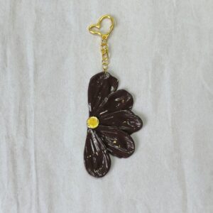 Colgador de bolso con forma de media flor, compuesta de 5 pétalos en color marrón oscuro con detalles iridiscentes El enganche tiene forma de corazón y es en color dorado
