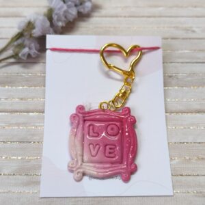 Charm/Llavero marco, en colores rosas degradados. En el interior pone Love